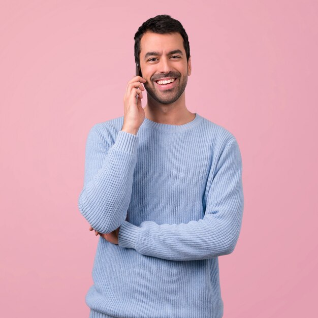 Mens met blauwe sweater die mobiele telefoon op roze achtergrond met behulp van