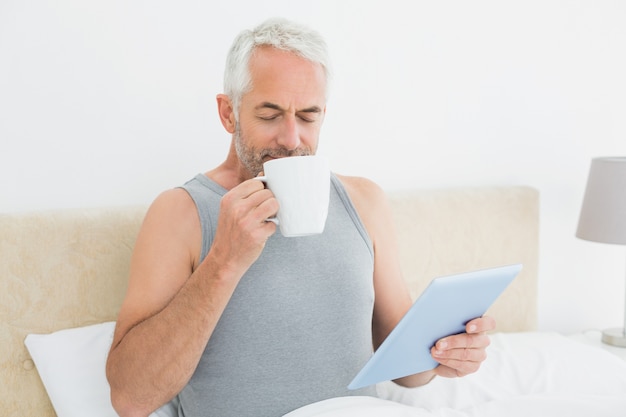 Mens met digitale tablet het drinken koffie in bed