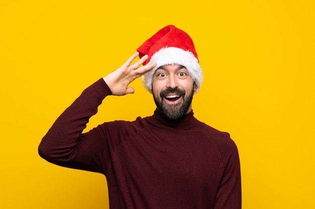 Mens met Kerstmishoed die verrassingsgebaar over geïsoleerde gele achtergrond doet