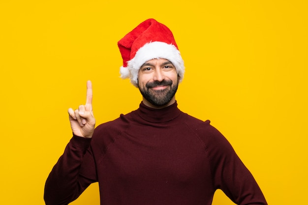 Mens met Kerstmishoed over geïsoleerde gele muur die en een vinger in teken van het beste tonen opheffen