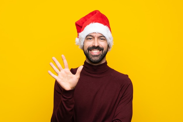 Mens met Kerstmishoed over geïsoleerde gele muur die vijf met vingers tellen