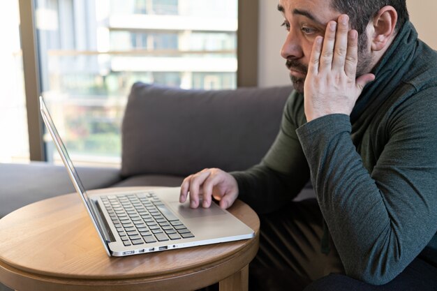 Mens thuis online werken of studie die laptop op bank met behulp van.