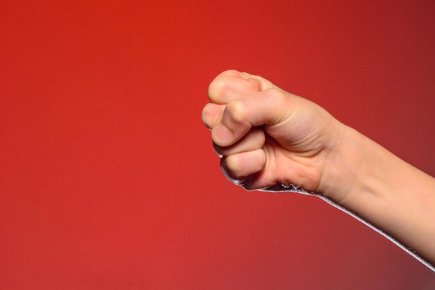 Menselijke hand die vingers in een vuist kneep die symbool staat voor haat en weerstand geïsoleerd op een rode achtergrond