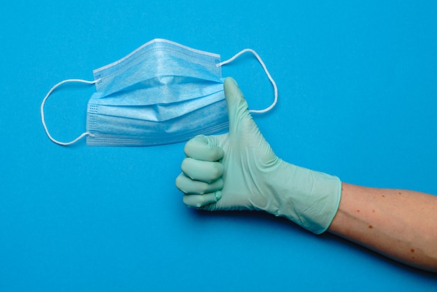 Menselijke hand in beschermende handschoen en gezichts beschermende maskers over blauwe muur