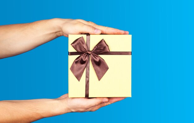 Menselijke hand met bruin lint verpakt vakantieverrassingsgeschenk of aanwezig doospakket op blauwe achtergrond