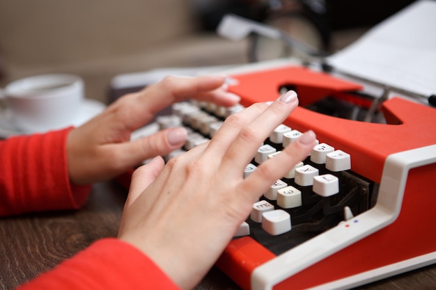 Menselijke handen die op rode typemachine schrijven