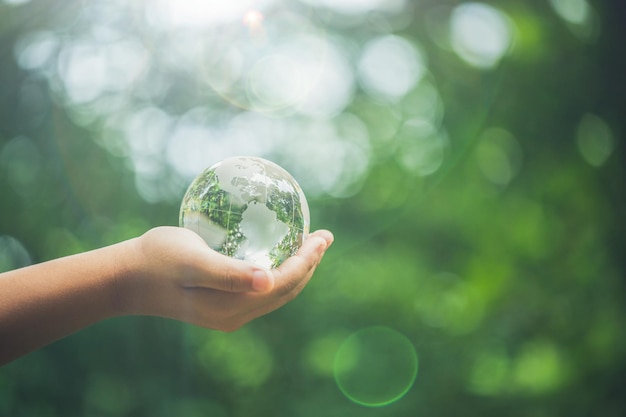 Menselijke handen met aarde bol kristal of duurzaam bol glas met zonlicht op groene natuur achtergrond in ecologie milieu bos concept van instandhouding milieubescherming planeet