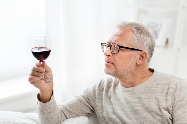 mensen, alcohol en dranken concept - senior man die thuis rode wijn drinkt uit glas