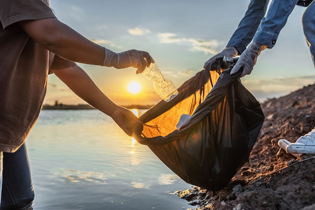 Mensen bieden vrijwilliger afval plastic fles aan in zwarte tas op rivier in zonsondergang