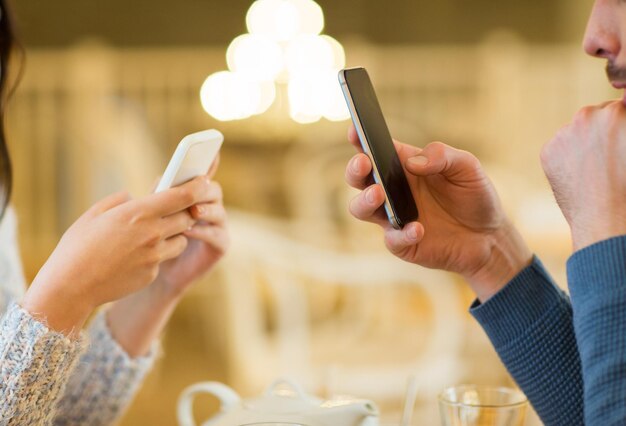 mensen, communicatie en technologie concept - close-up van paar met smartphones die thee drinken in café of restaurant