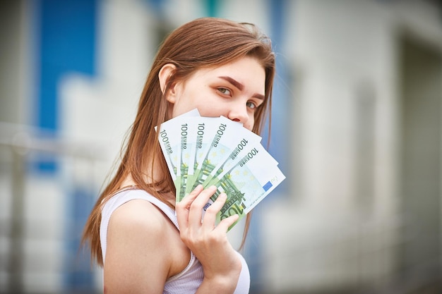 Mensen concept glimlachend tienermeisje in pullover met honderden eurobankbiljetten over grijze achtergrond