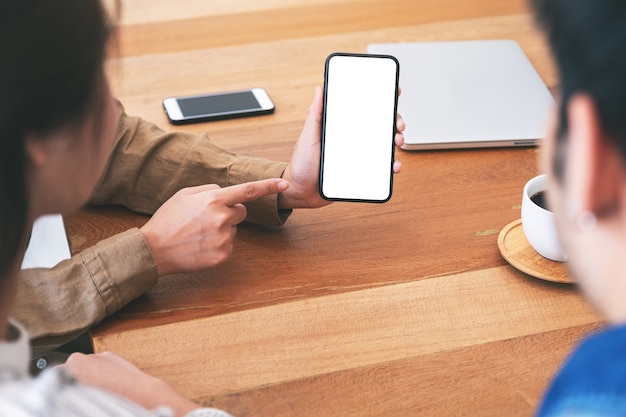 Mensen die dezelfde mockup-mobiele telefoon samen gebruiken en bekijken op houten tafel