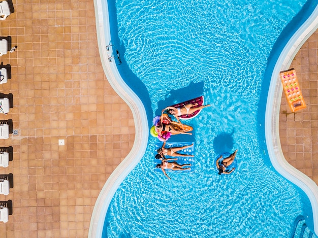 Mensen die plezier hebben in de zomer bij het zwembad met trendy gekleurde opblaasbare matras lilos