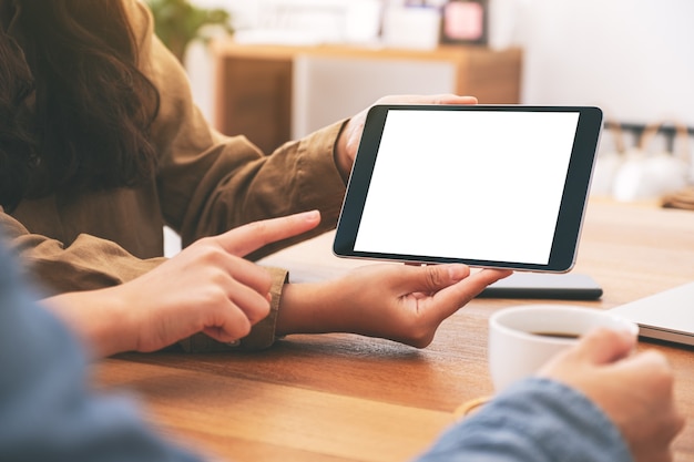 Mensen die samen dezelfde mockup-tablet-pc op houten tafel gebruiken, kijken en wijzen