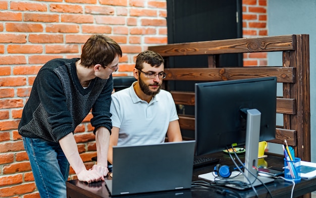 Mensen die werken en communiceren. twee zekere jonge mannen die laptop monitor bekijken