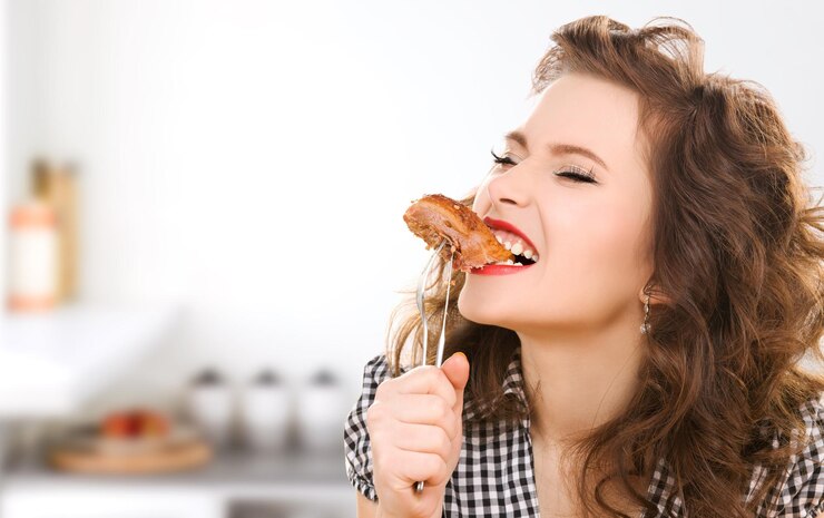 Foto mensen, dieet, culinair en voedselconcept - hongerige jonge vrouw die vlees op vork eet over keukenachtergrond