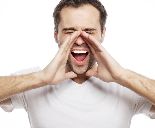 Mensen, emoties en lifestyle concept - knappe man in wit t-shirt die schreeuwt terwijl hij naar de camera kijkt en tegen een witte achtergrond staat