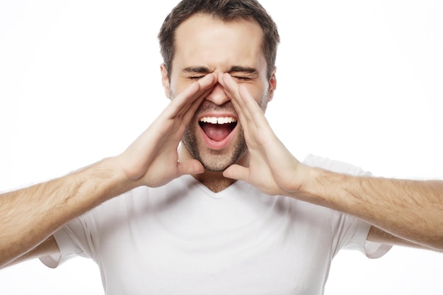 Mensen, emoties en lifestyle concept - knappe man in wit t-shirt die schreeuwt terwijl hij naar de camera kijkt en tegen een witte achtergrond staat