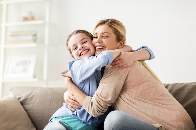 Mensen en familie concept - gelukkig lachend meisje met moeder knuffelen op de bank thuis