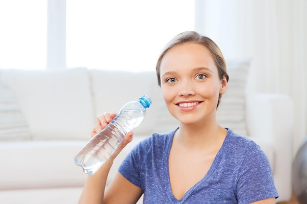 mensen en gezond levensstijlconcept - gelukkige vrouw met fles water thuis