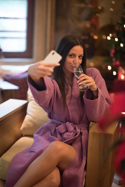 mensen en ontspanning concept mooie jonge vrouw in badjas champagne drinken en selfie doen in de spa over vakantie lichten achtergrond