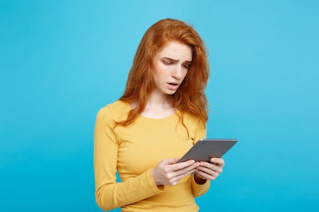 Mensen en technologie concept - close-up portret jonge mooie aantrekkelijke tedere ginger roodharige meisje schokkend en verdrietig op digitale tafel met wining iets. blauwe pastelachtergrond. kopieer de ruimte.