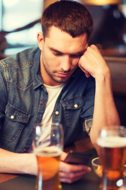 mensen en technologieconcept - man met smartphone die bier drinkt en leest of bericht verzendt in bar of pub