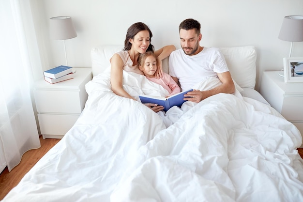 mensen, familie en ochtendconcept - gelukkig kind met ouders die boek in bed thuis lezen