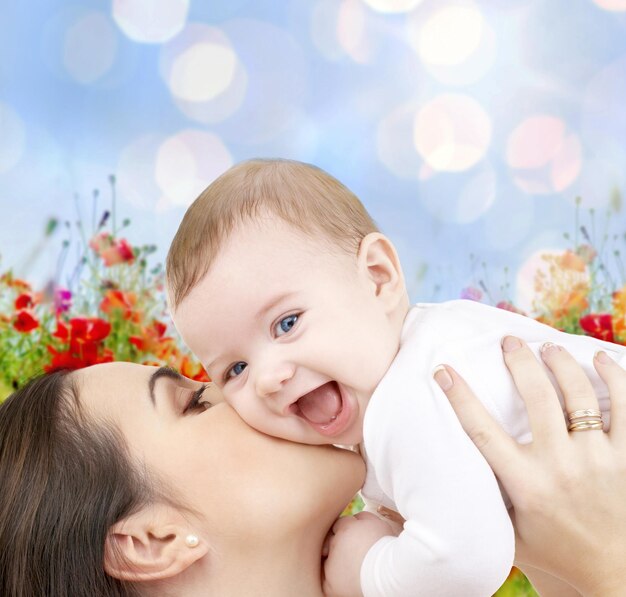 Mensen, familie, moederschap en kinderen concept - gelukkige moeder knuffelen schattige baby over blauwe lichten en papaverveld achtergrond