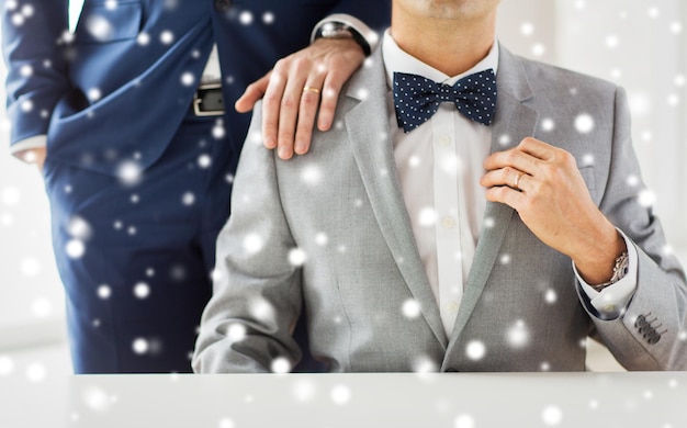Mensen, feest, homoseksualiteit, homohuwelijk en liefdesconcept - close-up van mannelijk homopaar met trouwringen bij hand op schouder leggen over sneeuweffect