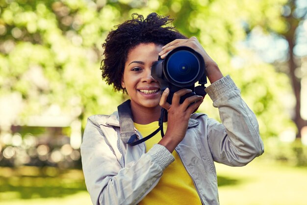 mensen, fotografie, technologie, vrije tijd en levensstijl - gelukkige jonge Afro-Amerikaanse vrouwelijke fotograaf op zoek naar digitale camerazoeker in zomerpark