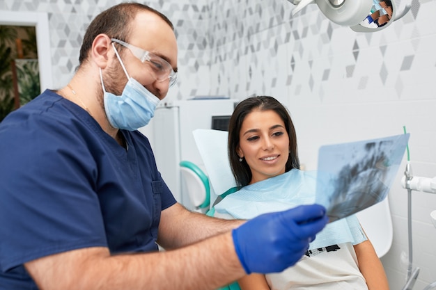 Mensen, geneeskunde, stomatologie en gezondheidszorgconcept - gelukkige mannelijke tandarts die werkplan toont aan vrouwelijke patiënt bij tandkliniekkantoor.