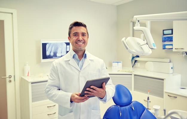 mensen, geneeskunde, stomatologie en gezondheidszorgconcept - gelukkige mannelijke tandarts van middelbare leeftijd in witte jas met tablet-pc-computer op het kantoor van de tandheelkundige kliniek