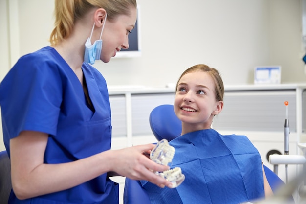 mensen, geneeskunde, stomatologie en gezondheidszorgconcept - gelukkige vrouwelijke tandarts die kaakmodel toont aan geduldig meisje op het kantoor van de tandheelkundige kliniek