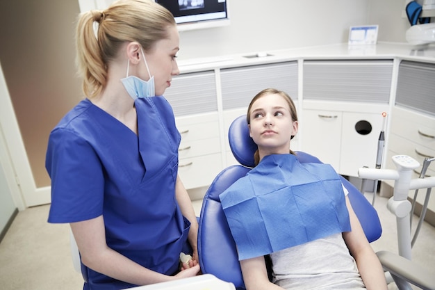 mensen, geneeskunde, stomatologie en gezondheidszorgconcept - gelukkige vrouwelijke tandarts met geduldig meisje die bij tandkliniekbureau spreken