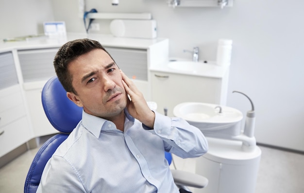 mensen, geneeskunde, stomatologie en gezondheidszorgconcept - ongelukkige mannelijke patiënt met kiespijn zittend op een tandartsstoel op het kantoor van de kliniek