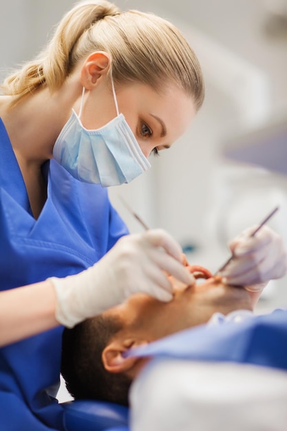 Foto mensen, geneeskunde, stomatologie en gezondheidszorgconcept - vrouwelijke tandarts met tandspiegel en sonde die de tanden van de mannelijke patiënt controleert op het kantoor van de tandheelkundige kliniek