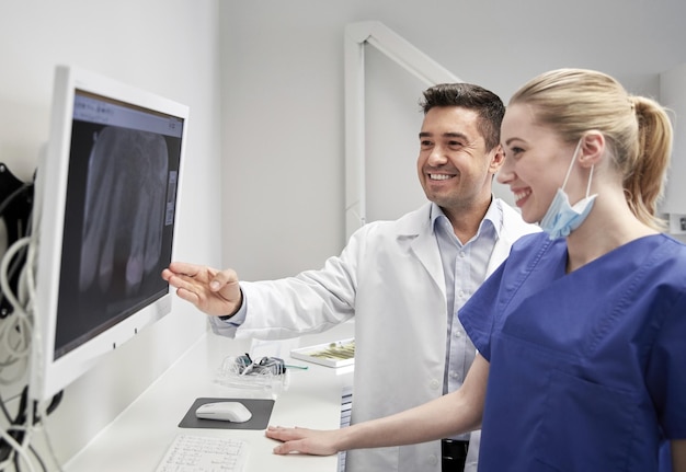 Foto mensen, geneeskunde, stomatologie, technologie en gezondheidszorgconcept - gelukkige tandartsen die op zoek zijn naar röntgenscan op monitor bij tandheelkundige kliniek