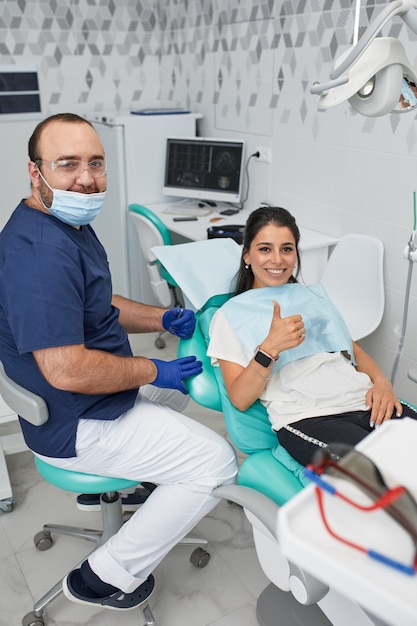 Mensen, geneeskunde, tandheelkunde en gezondheidszorgconcept - gelukkige mannelijke tandarts die werkplan toont aan vrouwelijke patiënt op het kantoor van de tandheelkundige kliniek