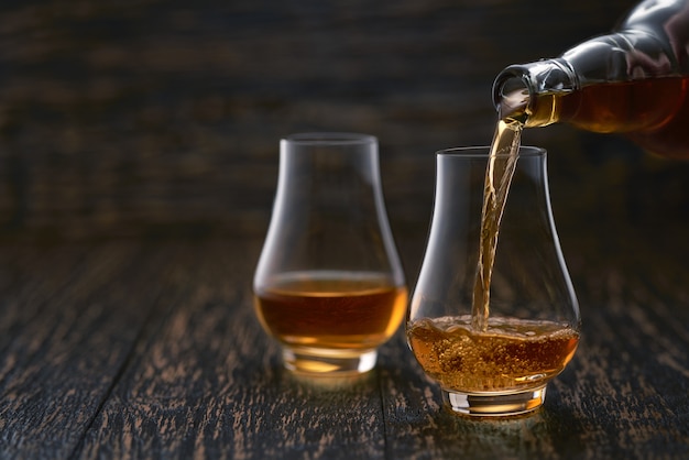 Mensen gietende whisky in glazen op rustieke houten lijst selectieve nadruk.