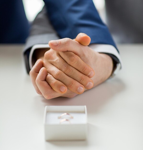 mensen, homoseksualiteit, homohuwelijk en liefde concept - close-up van gelukkige mannelijke homo paar hand in hand en trouwringen in vak op tafel