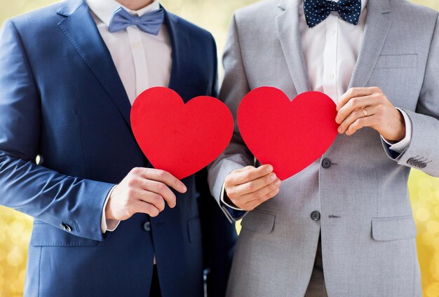 Mensen, homoseksualiteit, homohuwelijk, valentijnsdag en liefde concept - close-up van gelukkig getrouwd mannelijk homopaar met rode papieren hartvormen op bruiloft over gele lichten achtergrond