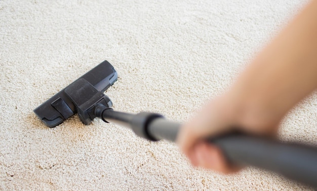 mensen, huishoudelijk werk en huishoudelijk concept - close-up van de hand met stofzuiger die tapijt thuis schoonmaakt