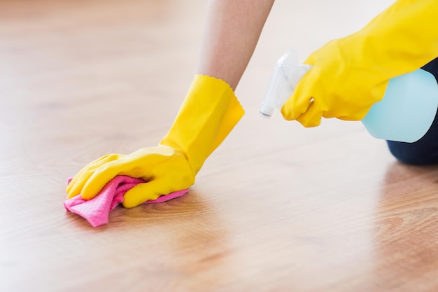 mensen, huishoudelijk werk en huishoudelijk concept - close-up van vrouw in rubberen handschoen met doek en wasmiddelspray die de vloer thuis schoonmaakt