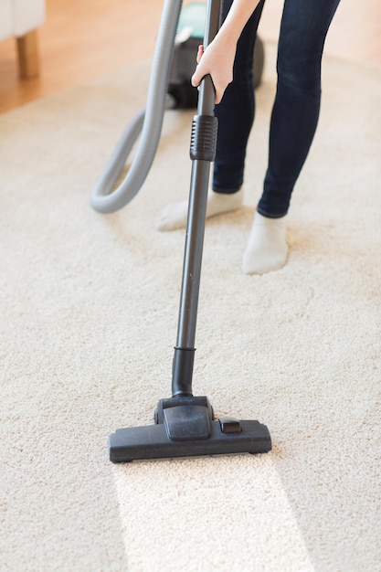 Mensen, huishoudelijk werk en huishouden concept - close-up van een vrouw met benen stofzuiger die tapijt thuis schoonmaakt