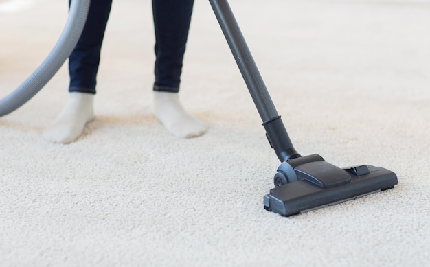 Mensen, huishoudelijk werk en huishouden concept - close-up van een vrouw met benen stofzuiger die tapijt thuis schoonmaakt