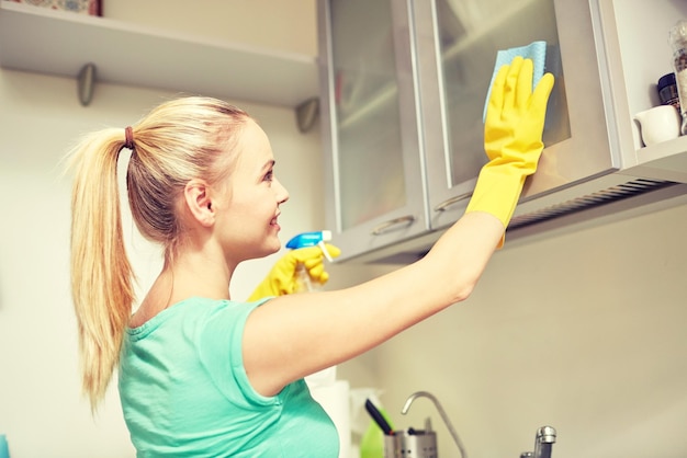 Foto mensen, huishoudelijk werk en huishoudenconcept - gelukkige vrouwenreinigingskast met vod en reinigingsmiddel thuis keuken