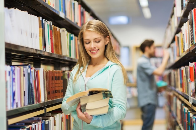 Mensen, kennis, onderwijs en schoolconcept - gelukkig studentenmeisje of jonge vrouw met boek in bibliotheek