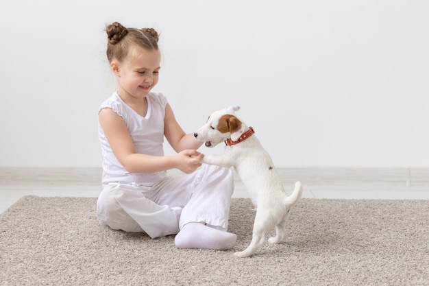 Mensen, kinderen en huisdieren concept - klein kind meisje zittend op de vloer met schattige puppy Jack Russell Terrier