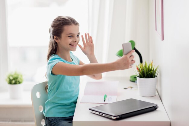 mensen, kinderen en technologieconcept - meisje met laptopcomputer en smartphone die selfie nemen of thuis videogesprek voeren